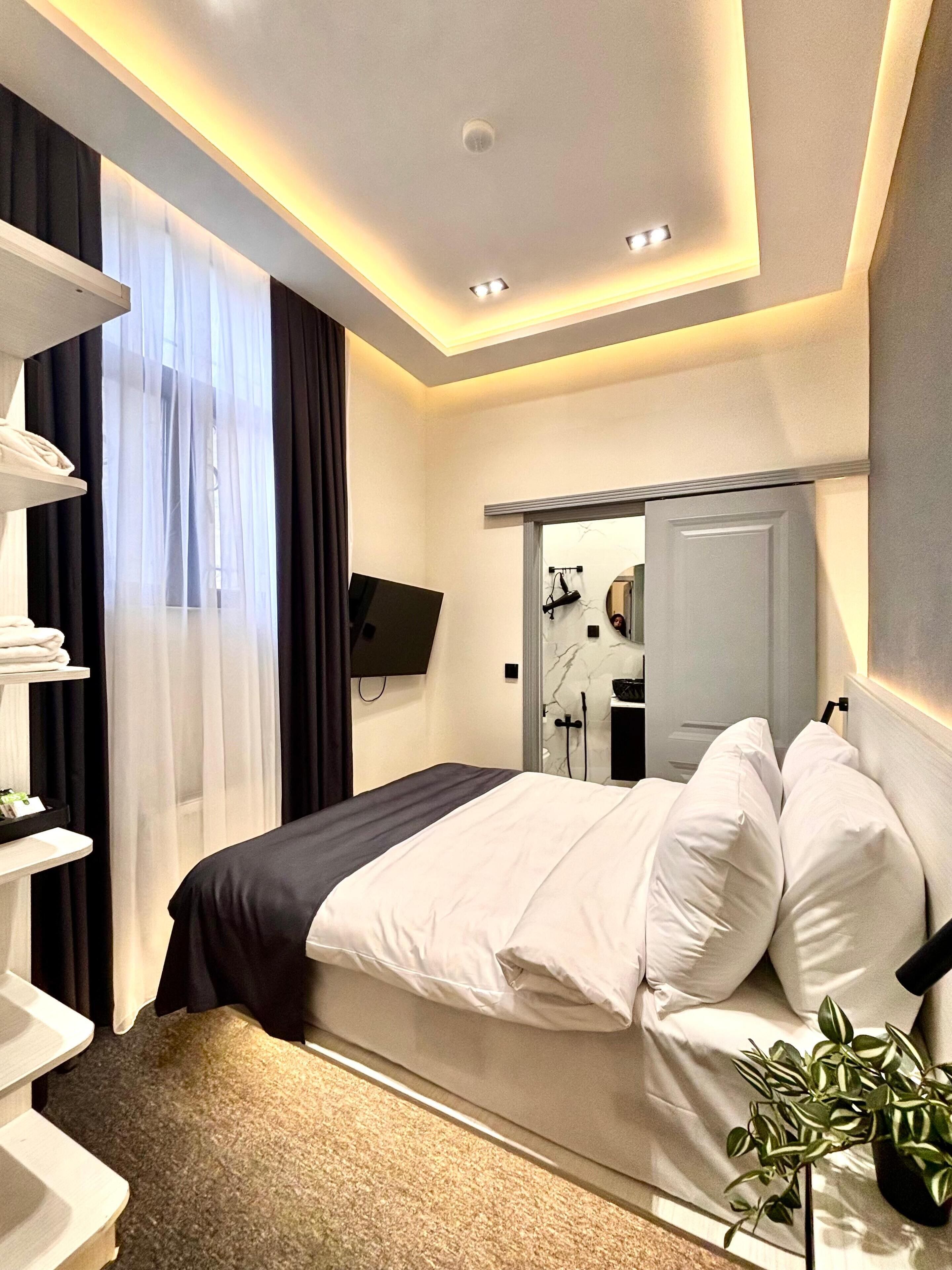 Ein modernes Hotelzimmer mit Bett, Fernseher, Spiegel und Pflanze.