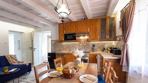 Een eetgedeelte met een houten tafel gedekt voor twee personen, een keuken met houten kasten, en een blauwe bank op de achtergrond.