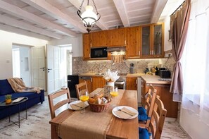 A dining area with a wooden table set for two, a kitchen with wooden cabinets, and a blue sofa in the background. - Romantic hideaway, private house with jacuzzi, sauna, free parking, AC, grill (Balatonalmádi)