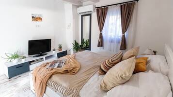 A modern bedroom with a bed, TV, and plants.