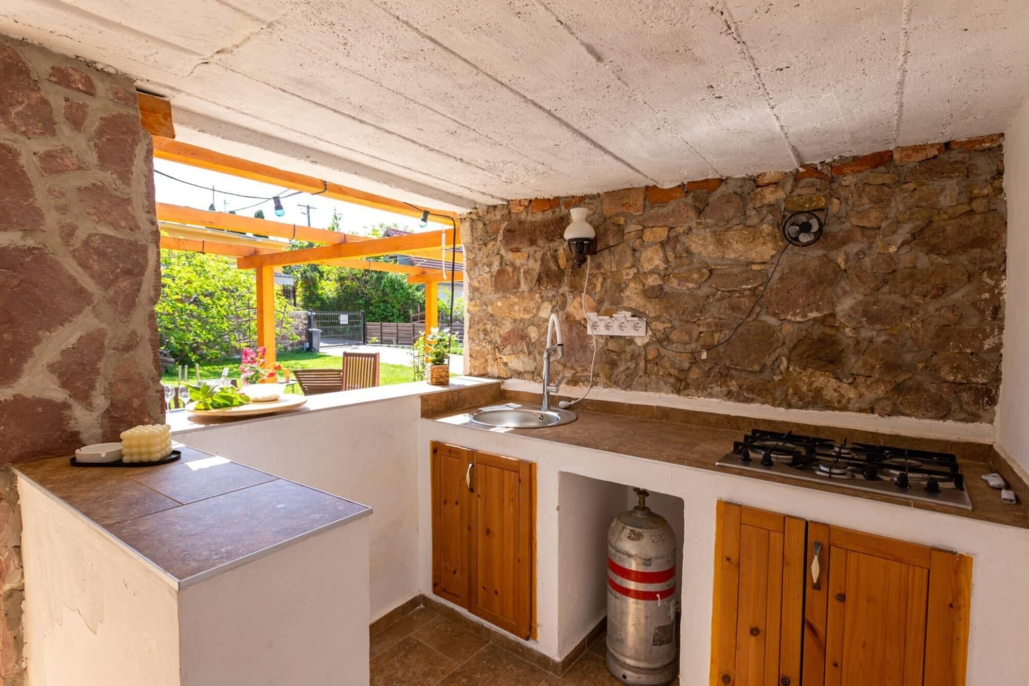 Une cuisine avec un mur en pierre, une cuisinière à gaz, un évier et des armoires en bois.