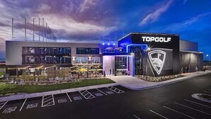 Un centre TopGolf moderne, doté d’un grand parking et d’une entrée bien éclairée.