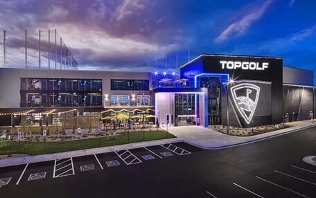 A modern TopGolf facility with a large parking area and a well-lit entrance.