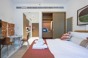 Hotellihuone, jossa on sänky, työpöytä, tuoli, vaatekaappi ja kylpyhuone, joka näkyy avoimesta ovesta.
