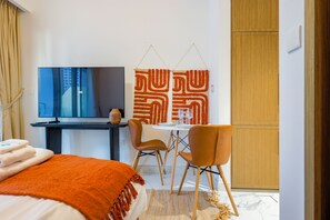 Una habitación de hotel moderna con cama, escritorio, televisor, silla y armario.