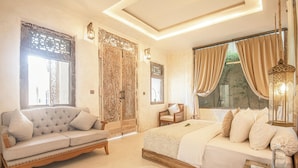 Een slaapkamer met een groot bed, een bank en een stoel. Er is een raam met gordijnen en een decoratief wandpaneel.