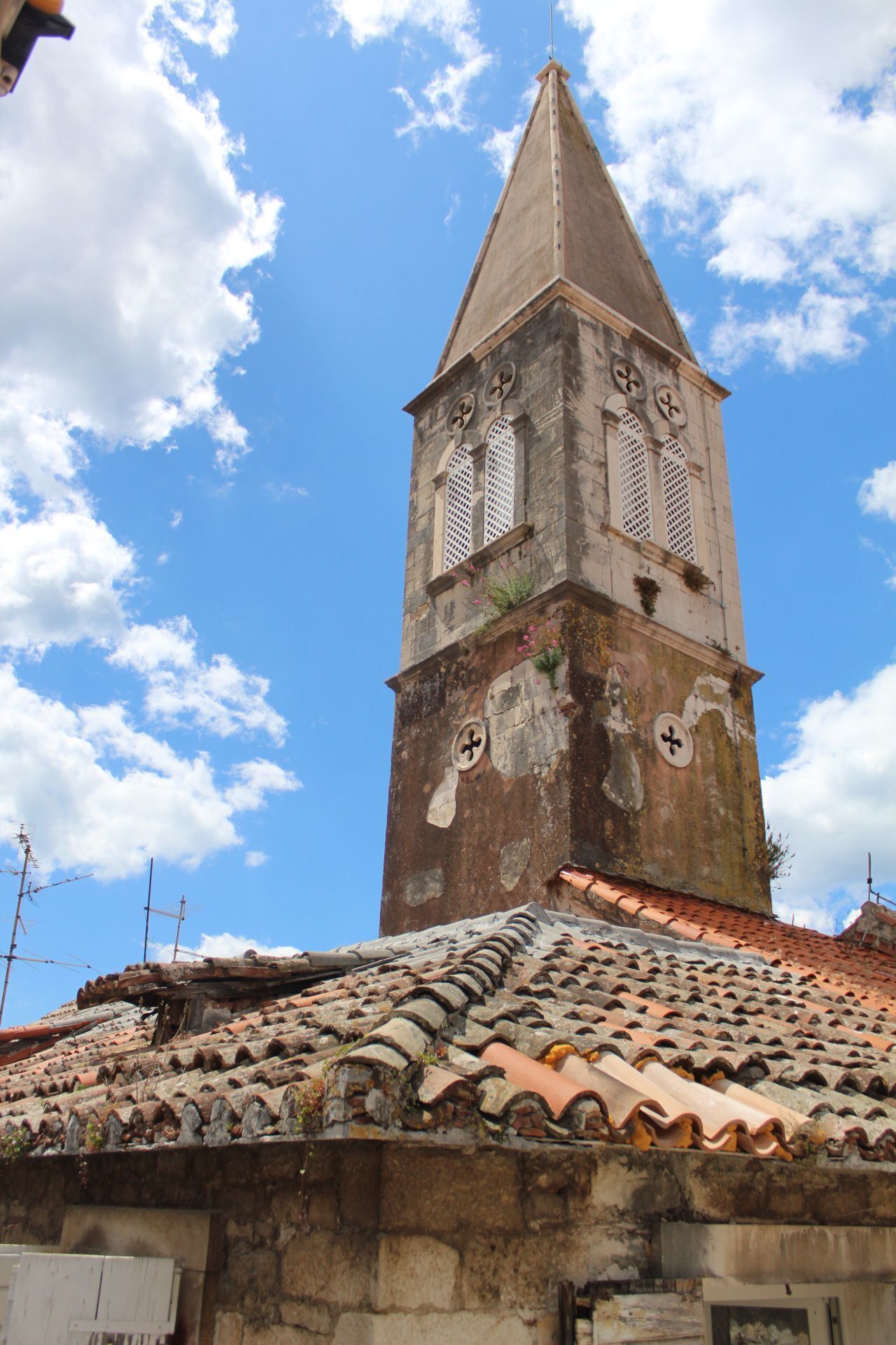 Una torre histórica con un techo empinado y dos ventanas de arco, sobre un cielo azul despejado.