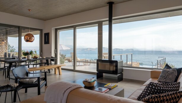 A modern living room with a large TV, comfortable seating, and a view of the sea.