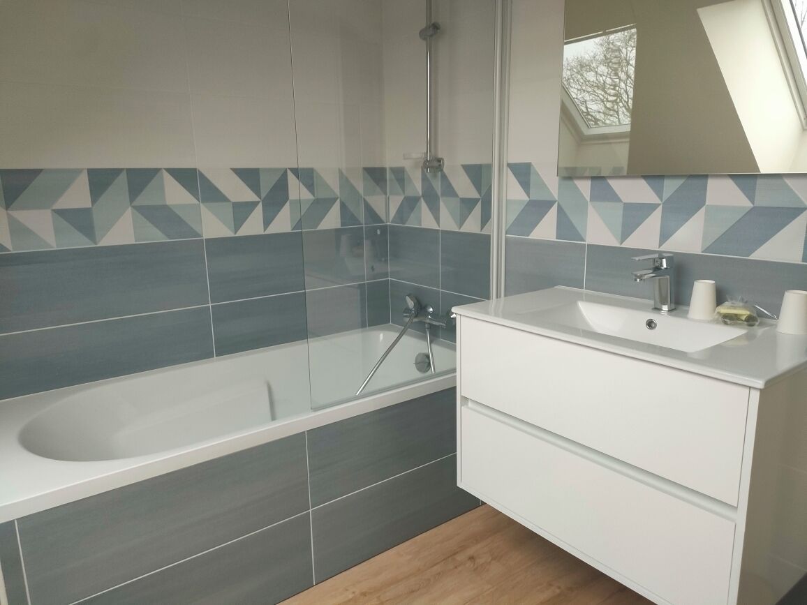 A modern bathroom with a glass-enclosed bathtub, a white vanity with a mirror, and a geometric tile backsplash.