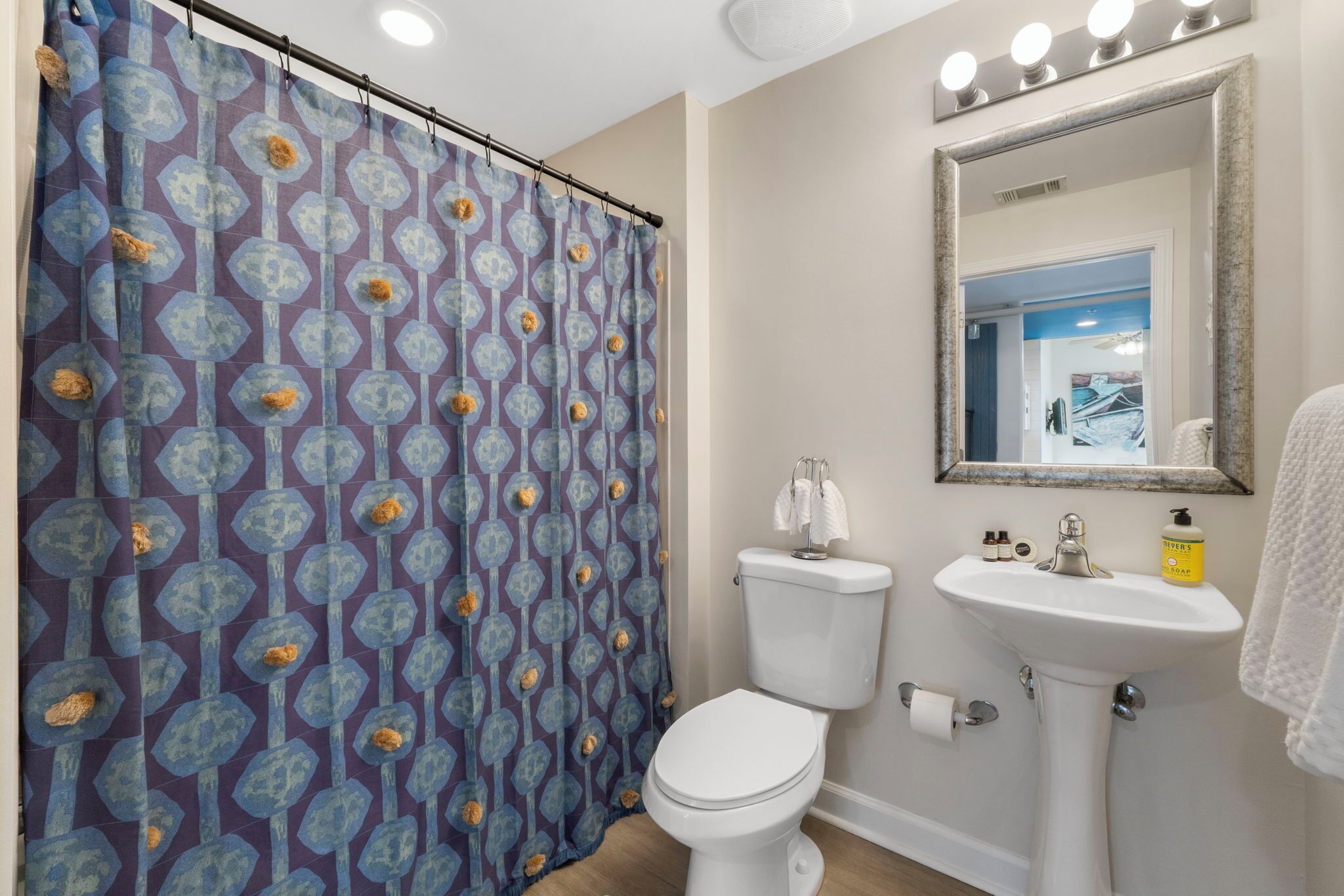 A bathroom with a patterned shower curtain, a toilet, a sink with a mirror above it, and a towel rack.
