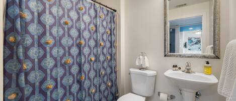 A bathroom with a patterned shower curtain, a toilet, a sink with a mirror above it, and a towel rack.