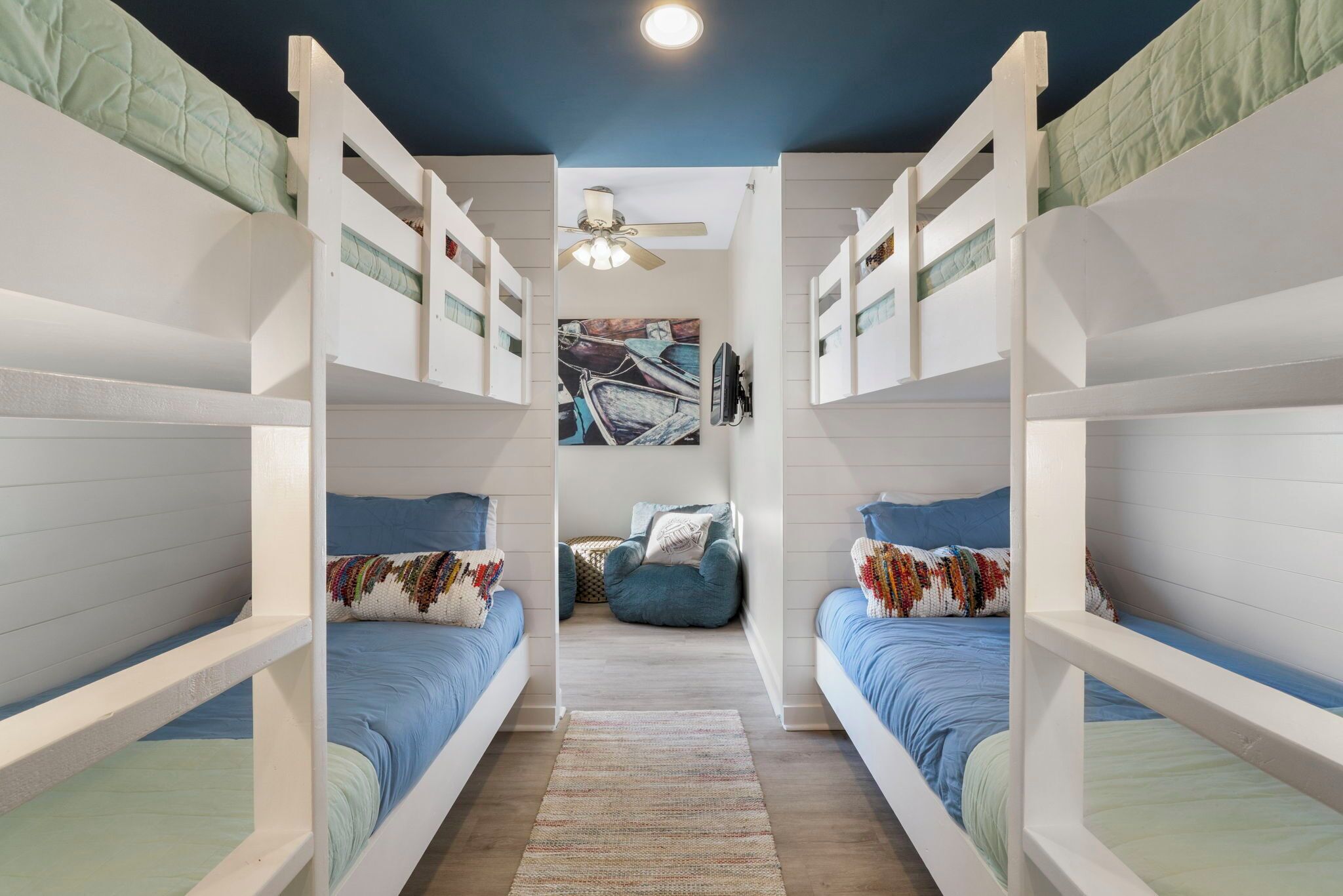 Habitación con literas, ventilador de techo, alfombra y un cuadro en la pared.