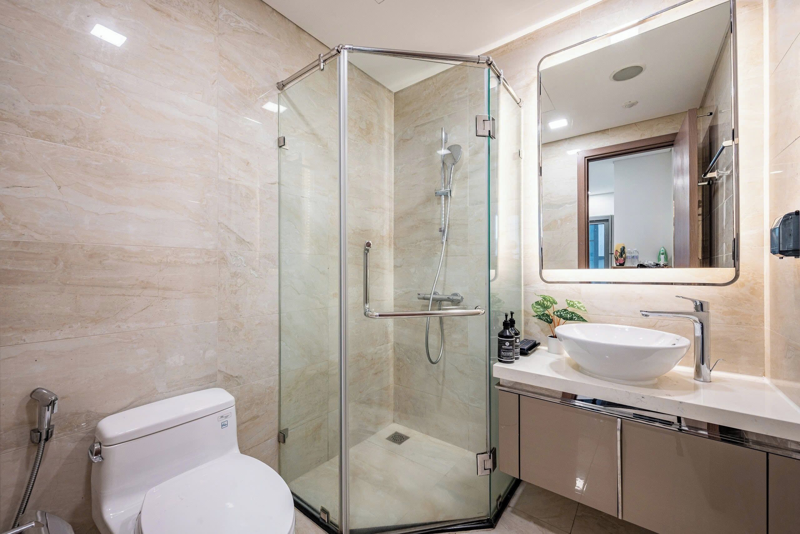 Un baño moderno con ducha de vidrio, lavamanos blanco y un espejo grande.