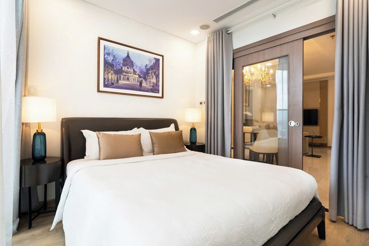 Ein Hotelzimmer mit einem großen Bett, zwei Nachttischen mit Lampen, einem Gemälde an der Wand und einer Schiebetür zu einer Sitzecke.