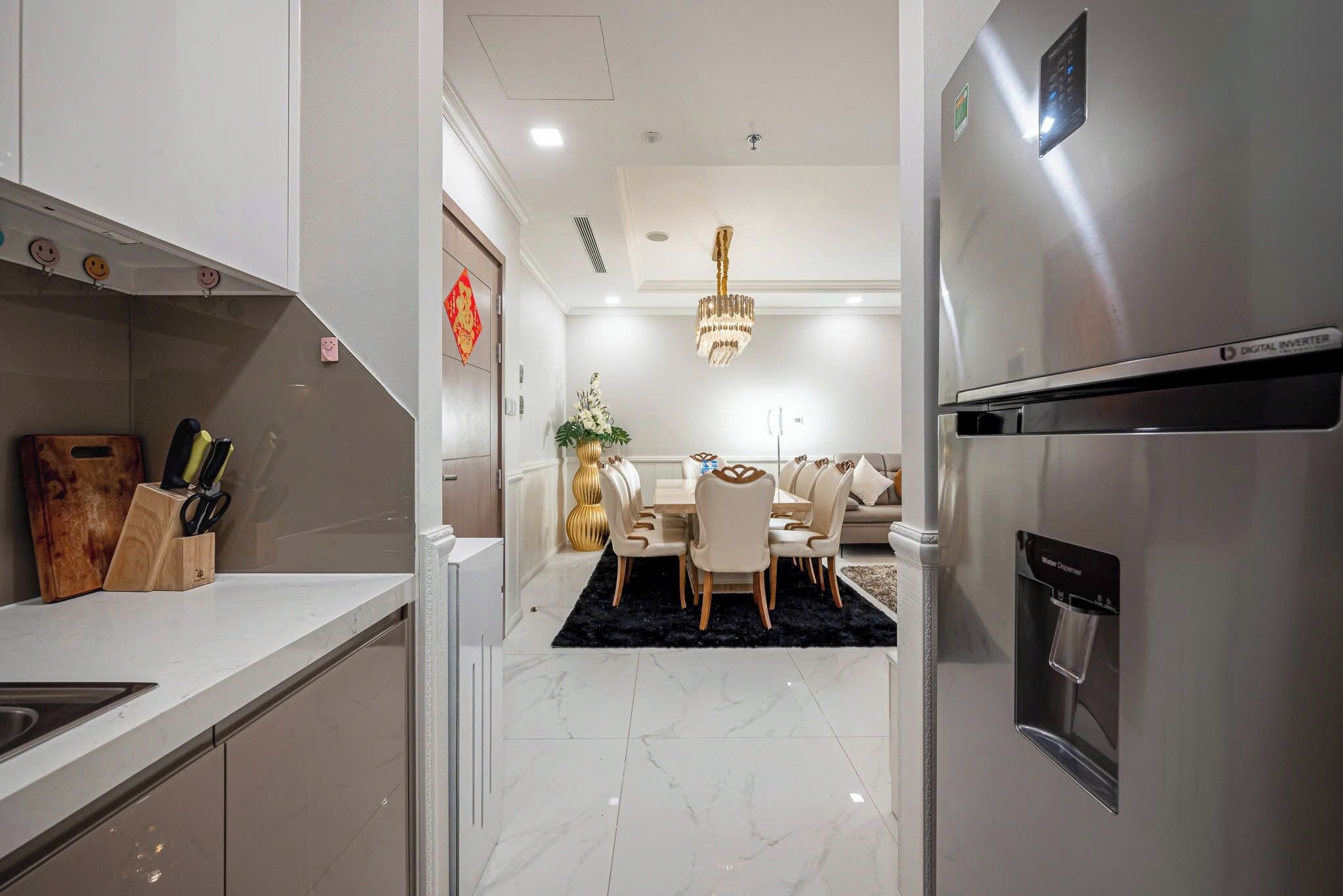 A modern kitchen with a water dispenser, a dining area with a chandelier, and a digital inverter refrigerator.
