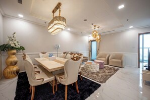 Ein moderner Essbereich mit großem Tisch und Stühlen, einer Chandelieber und einer Couch in einem hellen Raum mit großen Fenstern.