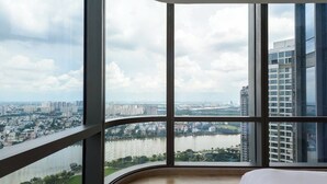 Ein Hotelzimmer in einem Hochhaus mit einer gewölbten Glasschrankwand, das einen weiten Panoramablick auf die Stadt und den Fluss bietet.