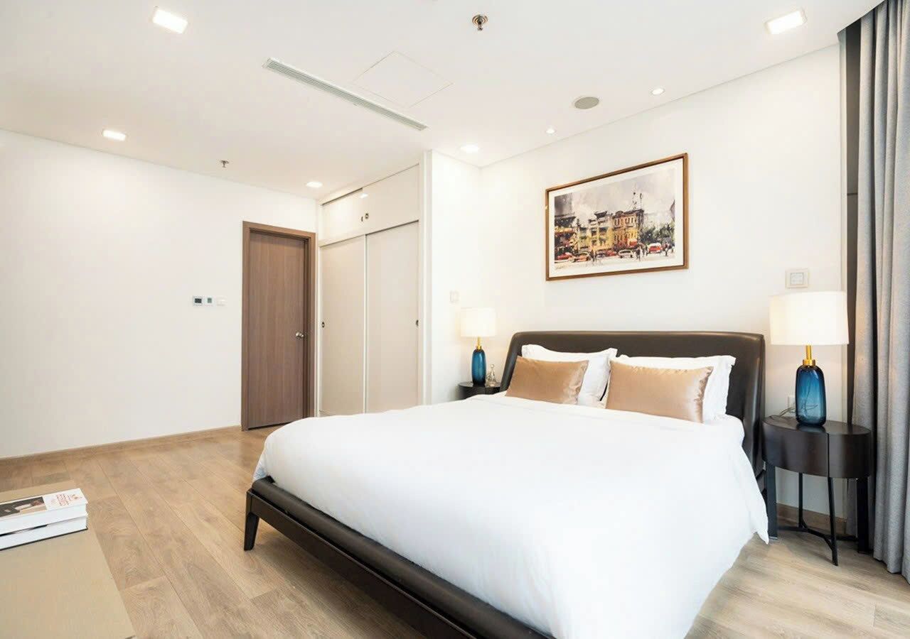 Habitación de hotel con una cama grande, dos mesitas de noche con lámparas, una puerta y un cuadro enmarcado en la pared.