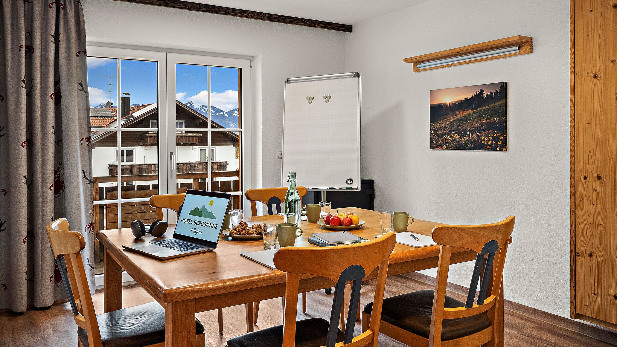 Uma sala de conferências com mesa de madeira, cadeiras, um laptop, um quadro branco e uma janela com vista para as montanhas.