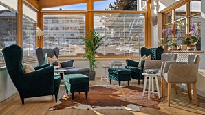 Una habitación luminosa con ventanas amplias, diversas opciones de asientos y una planta en el centro.