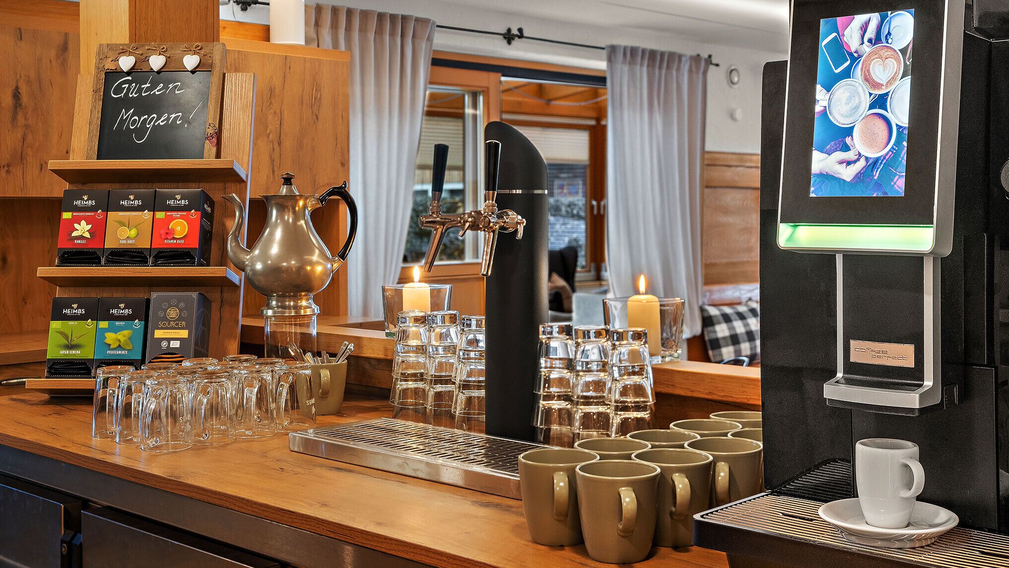 Un bar de café con una máquina de café, tetera y varios recipientes para café. También hay vasos y tazas en la barra.