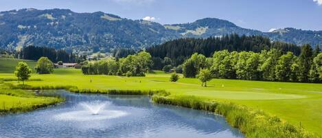 A golf course with a pond, trees, and mountains in the background.