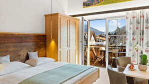 Un dormitorio con techo de madera, una cama, un armario, una mesa con una silla y vistas a un paisaje montañoso a través de un ventanal.