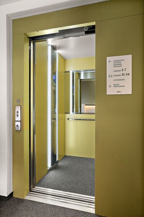 Un ascenseur avec une signalétique indiquant les numéros des chambres 1 à 7 et 11 à 14, un sauna et un espace de coworking.