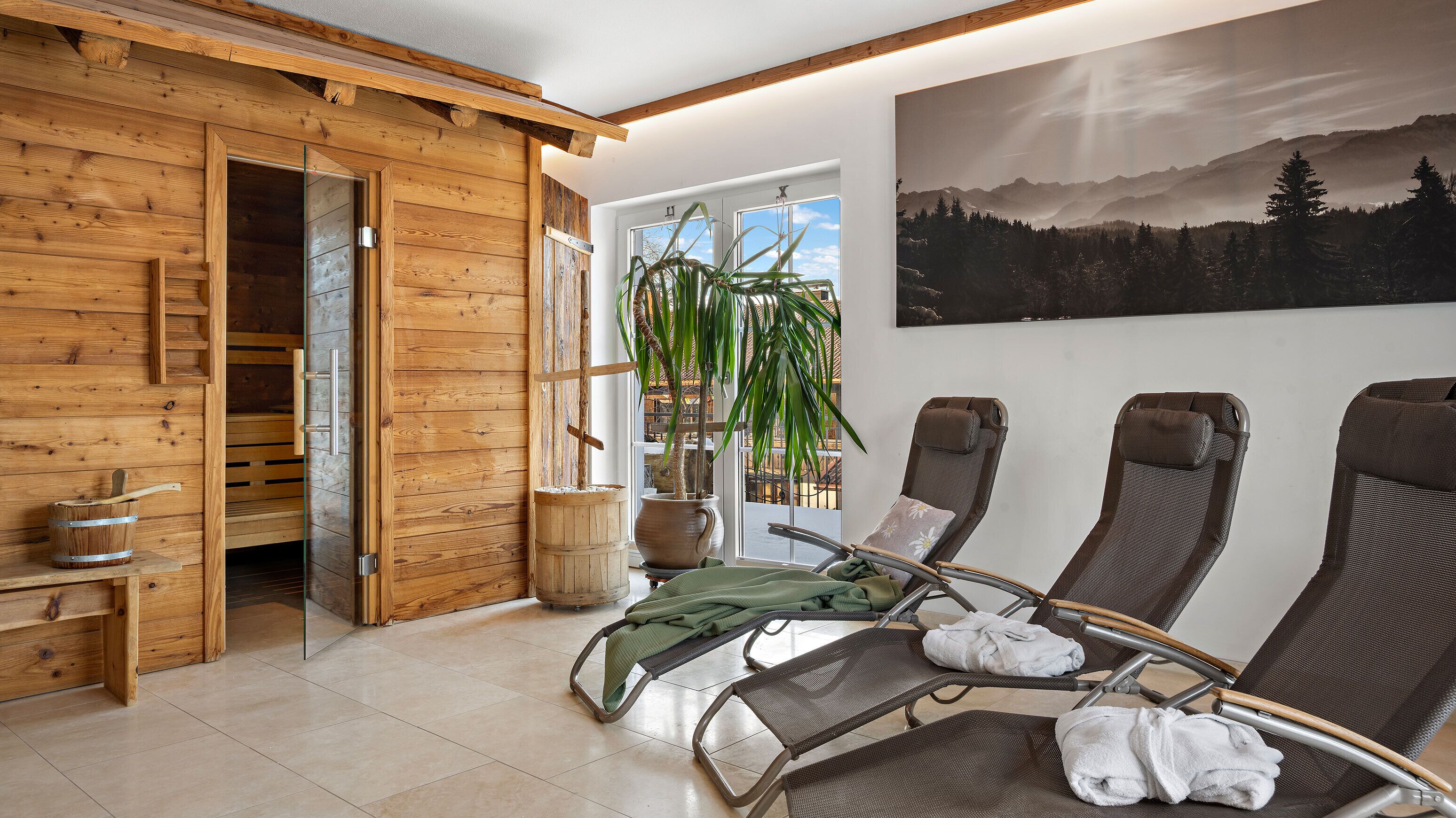 Ein Holzblockhaus-Interieur mit Sauna, einem großen Fenster mit Bergblick und einem Waldgemälde.
