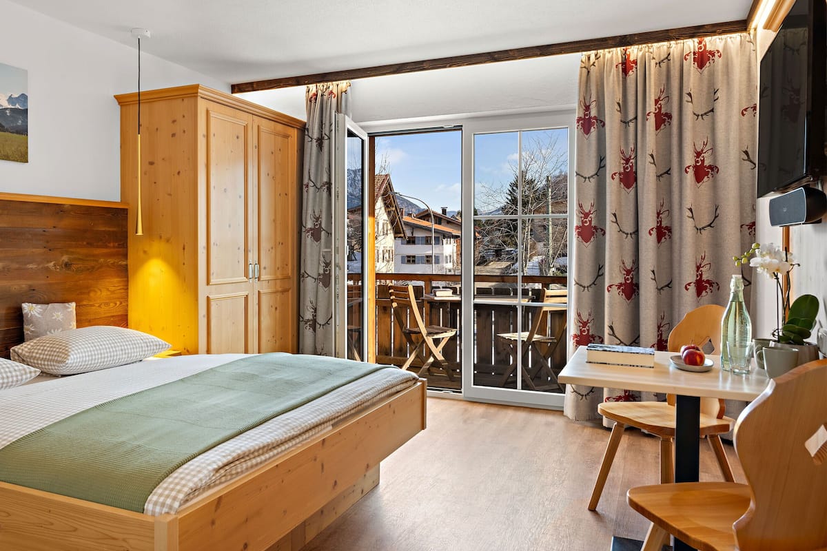 A bedroom with a wooden bed, a view of a balcony, and a dining area with a table and chairs.