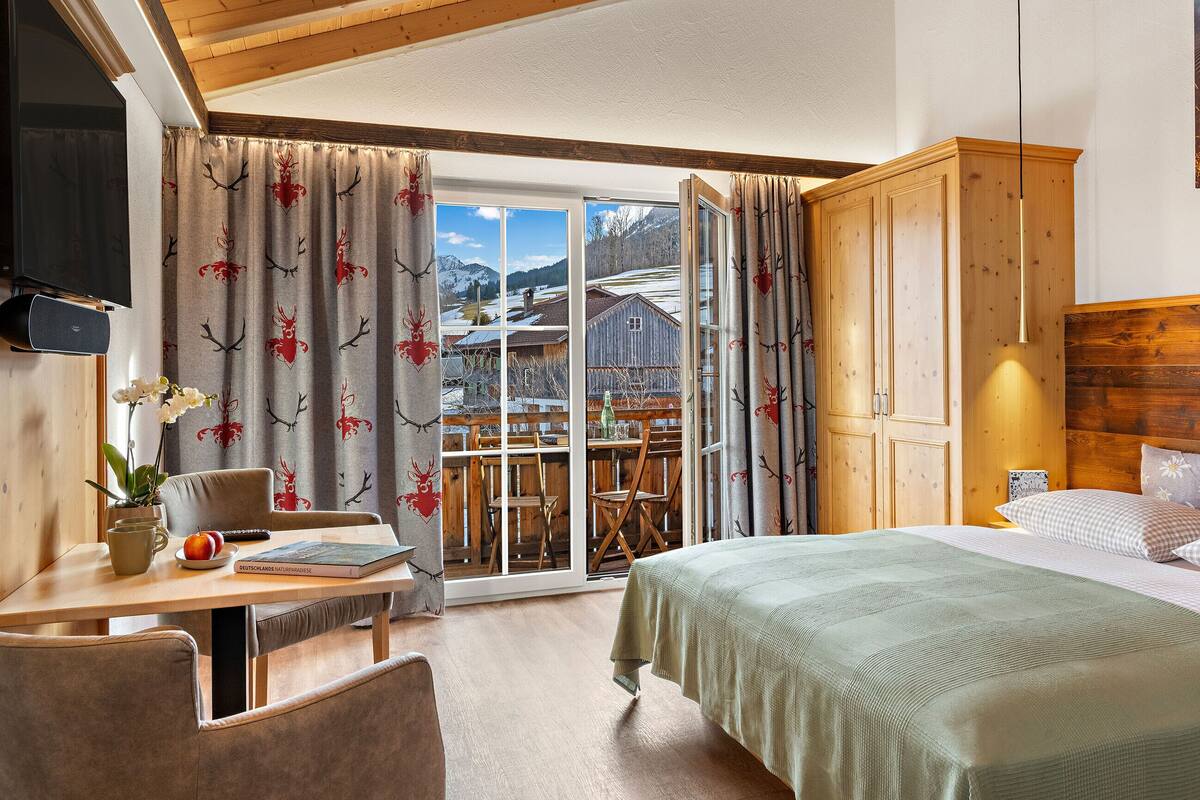 A hotel room with a bed, a desk with a chair, a TV, and a view of a mountain landscape.