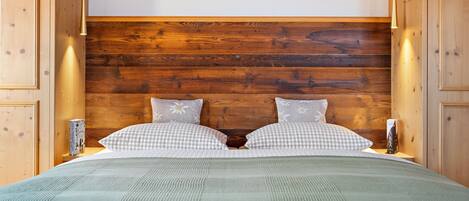 Quarto com cabeceira de madeira, almofadas xadrez e colcha verde.