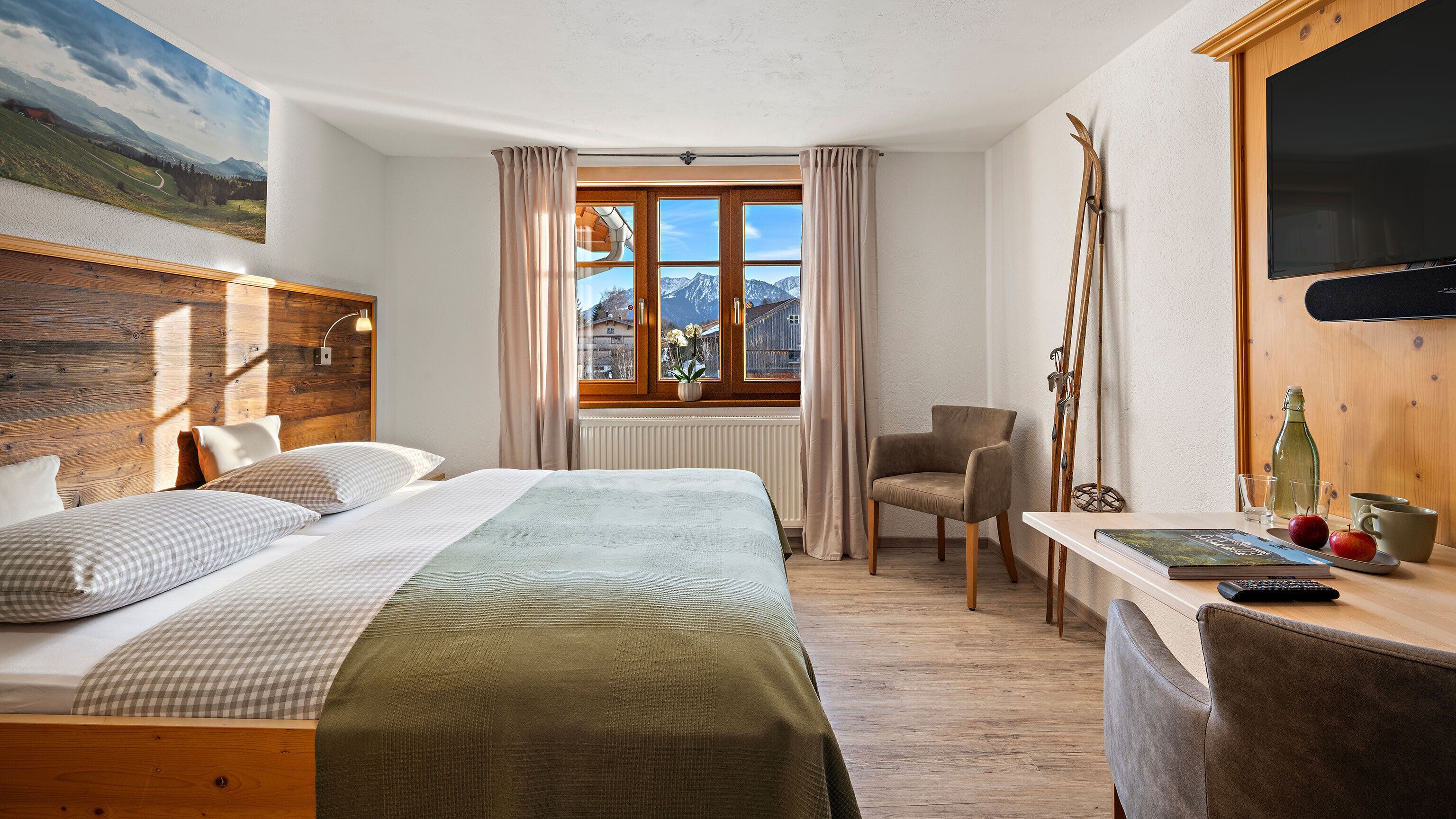 Une chambre d’hôtel avec un lit, une chaise, une table sur laquelle se trouvent une bouteille, des verres et des pommes.