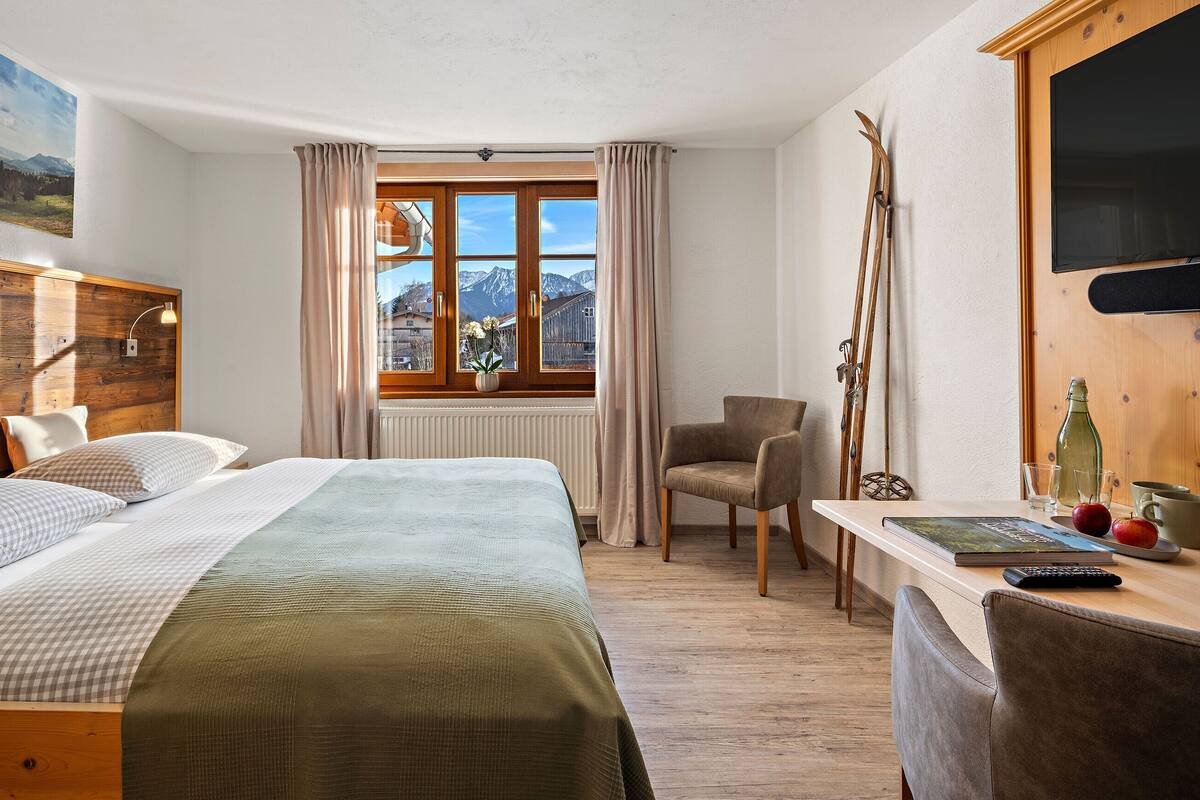 A hotel room with a bed, a chair, a table with a bottle, glasses, and apples.