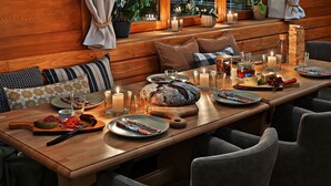 Una mesa de comedor de madera dispuesta con platos, cubiertos y velas, rodeada de sillas tapizadas.