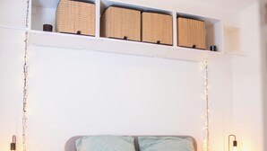 Ein Schlafzimmer mit einem Bett, zwei Nachttischen, einem Wandregal mit Körben und einer Pendelleuchte.
