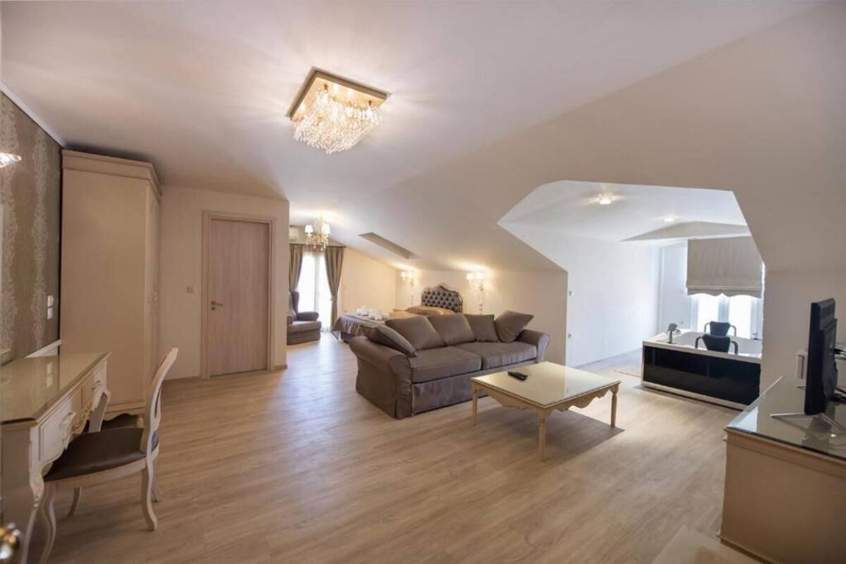 Un salón amplio con sofá, mesa de centro y televisor. Cuenta con una zona de comedor con mesa y sillas. El suelo es de madera y tiene una araña.