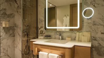A modern bathroom with a marble floor, a glass shower enclosure, a vanity with a sink, and a large mirror with a light.