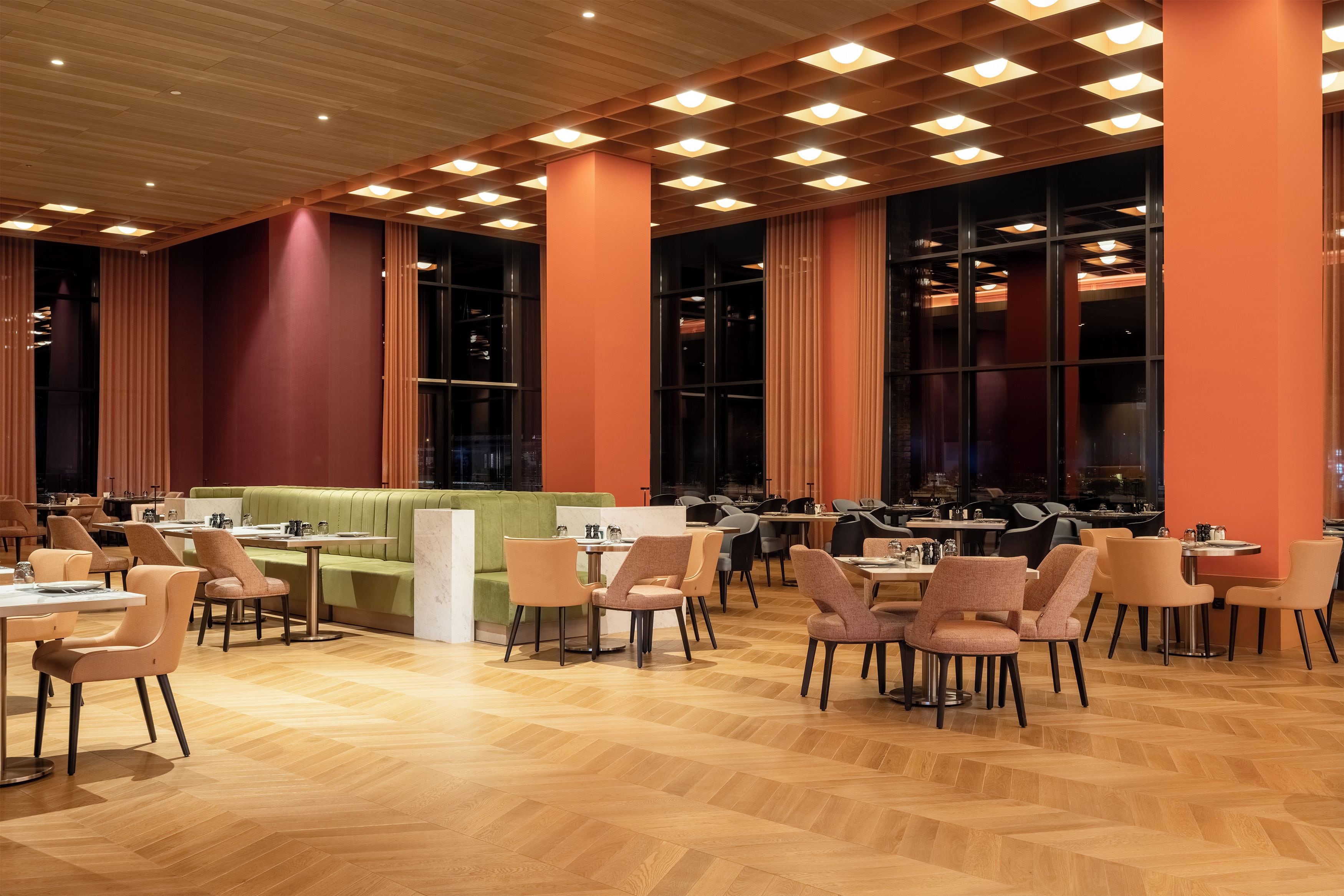 A spacious dining area with multiple tables and chairs, a green booth seating area, and large windows allowing natural light.