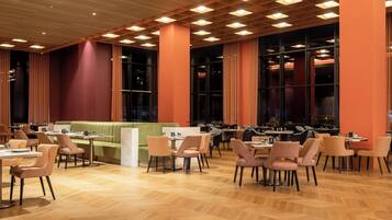 A spacious dining area with multiple tables and chairs, a green booth seating area, and large windows allowing natural light.
