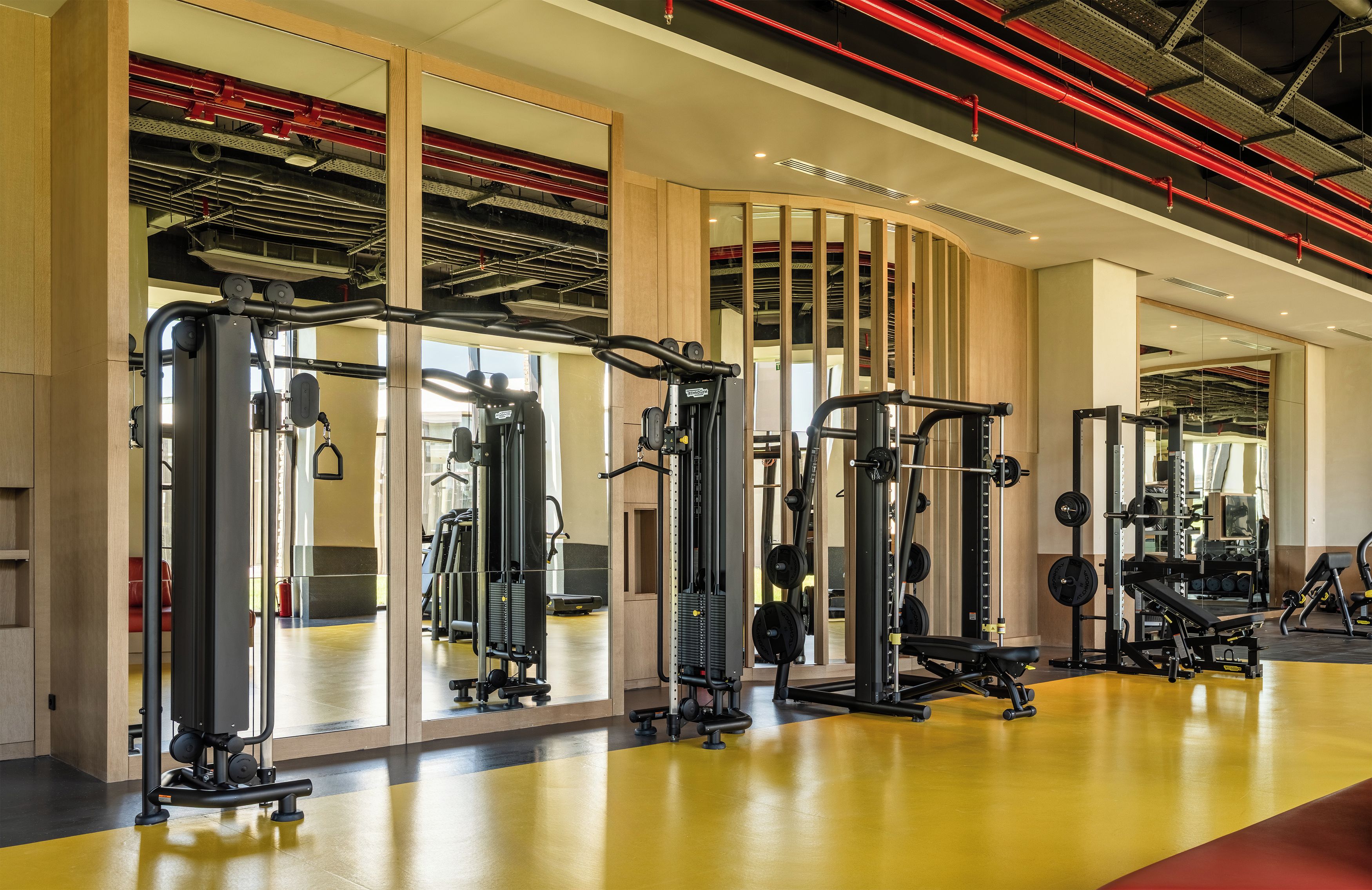 A modern gym with various exercise equipment, large mirrors, and a yellow floor.