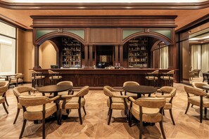Un área de bar con mostrador de madera, varias estanterías llenas de botellas y sillones de cuero dispuestos alrededor de mesas.