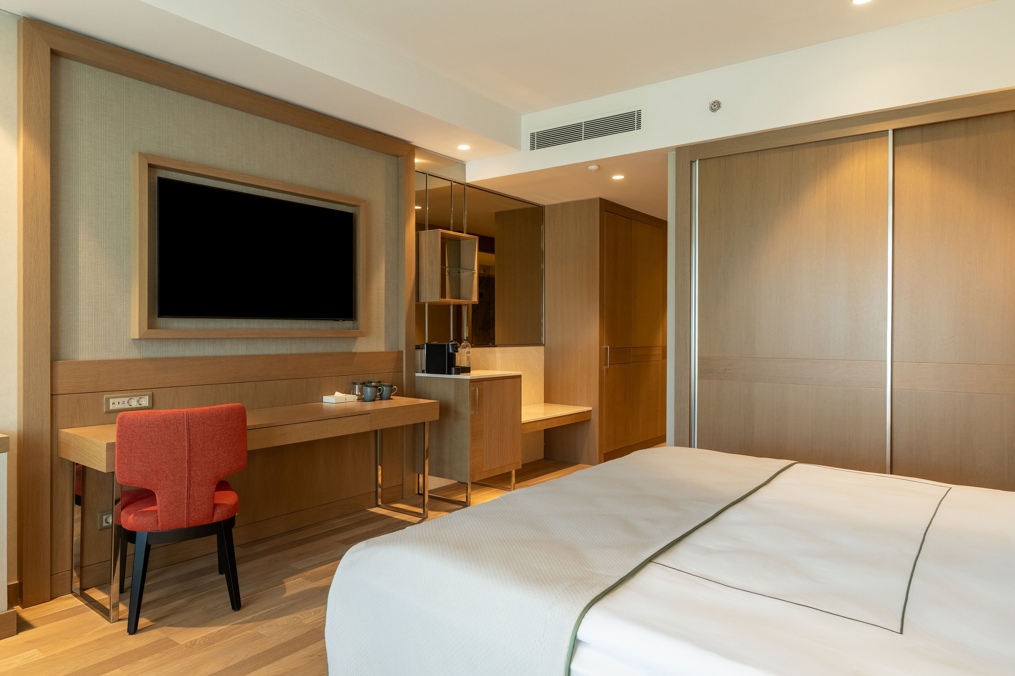 A hotel room with a bed, a desk, a chair, a television, and a wardrobe.