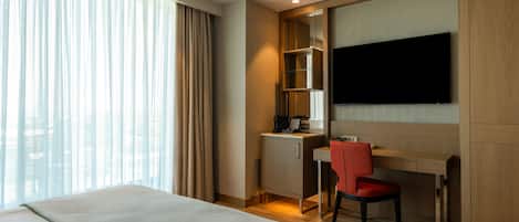 Habitación de hotel con cama, escritorio y silla, televisión y ventana con cortinas.