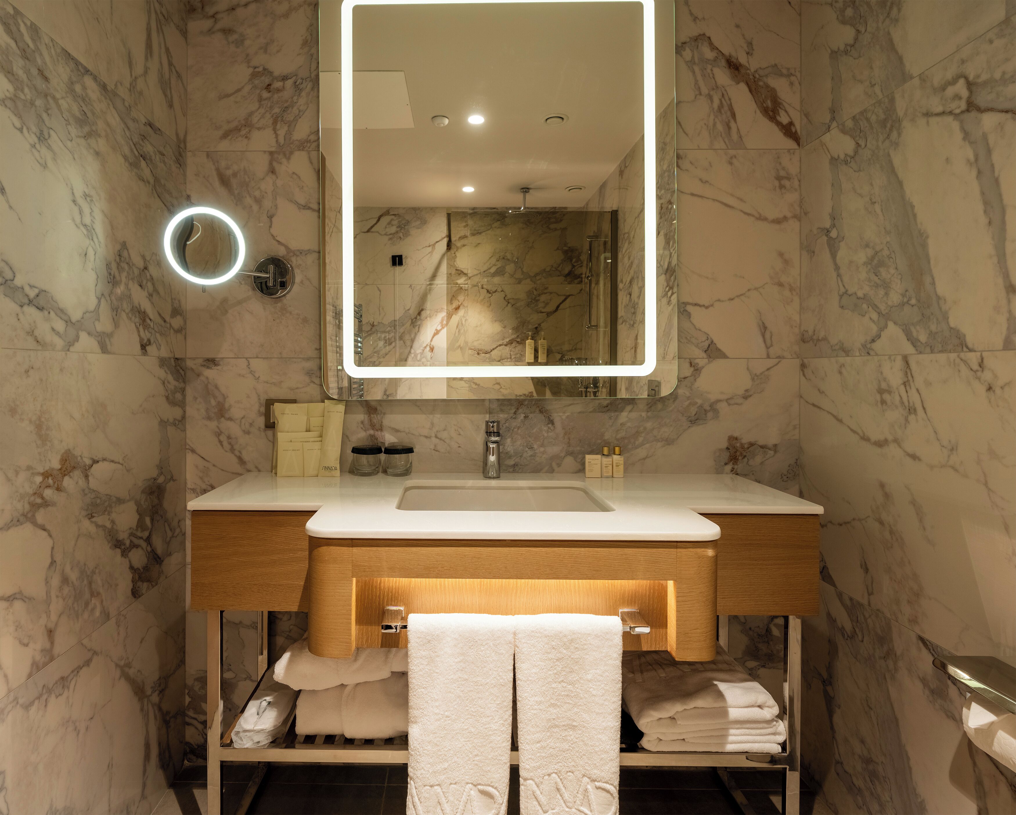 Un baño con pared de mármol, lavamanos con espejo y toallas.