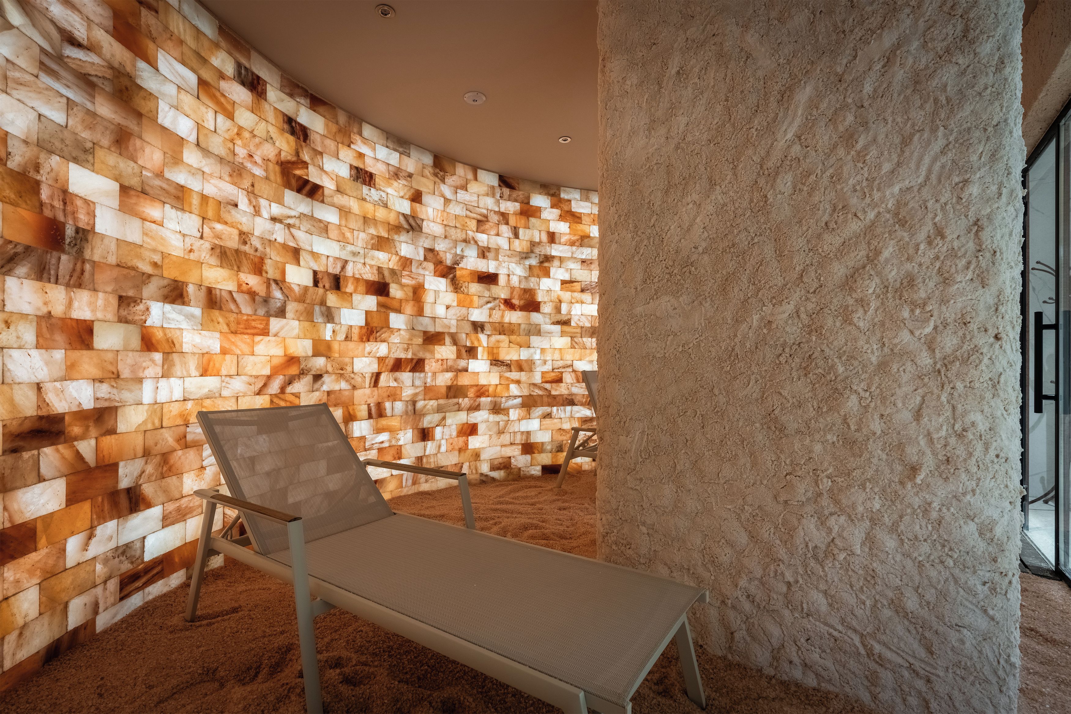 Un área de descanso con una pared curva de bloques texturizados, un sillón individual y un pilar con textura.