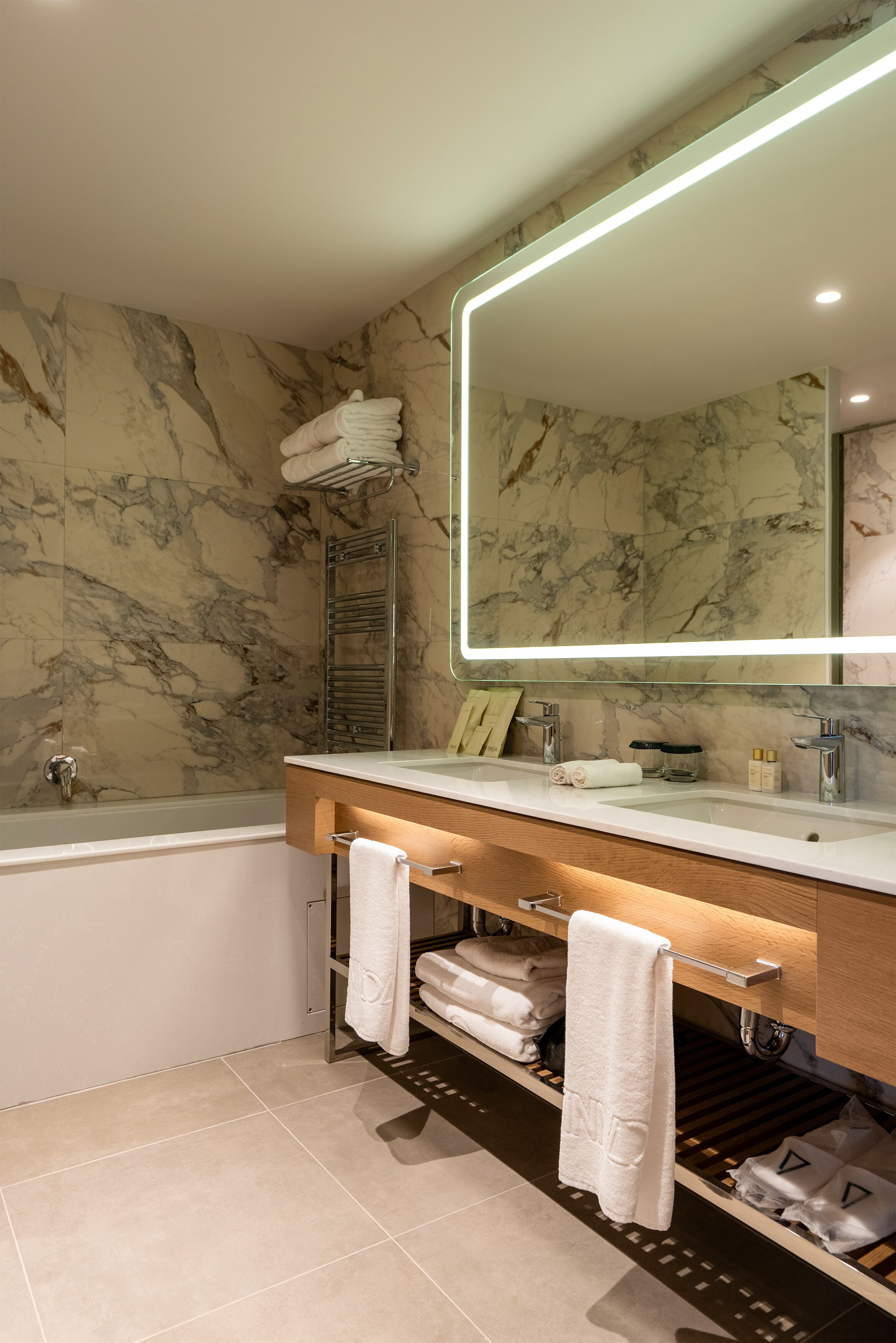Un baño moderno con pared de mármol, bañera integrada, tocador con espejo y un perchero para toallas.