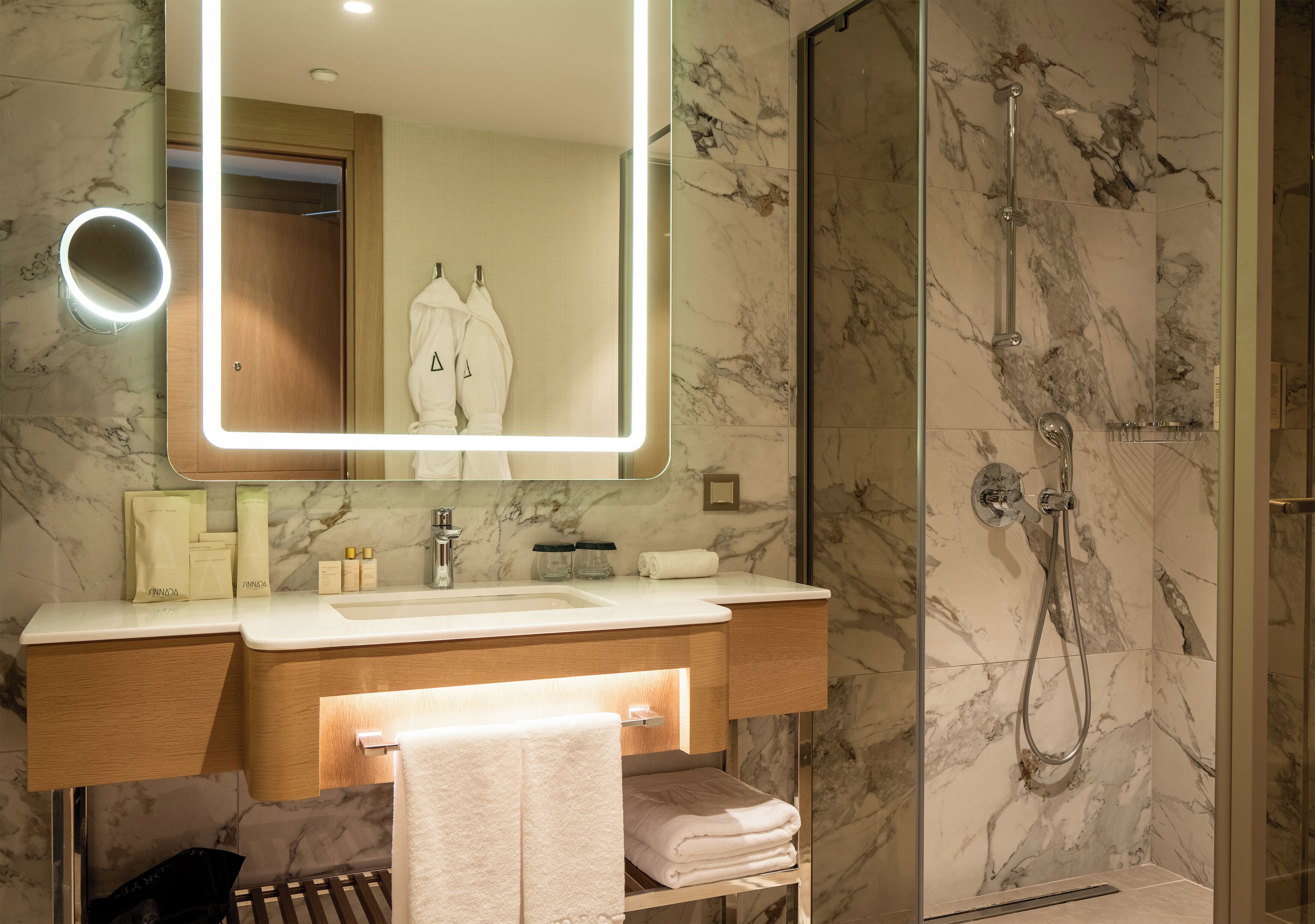 Een badkamer met een marmeren douche, een wastafel met spiegel en een handdoekrek.