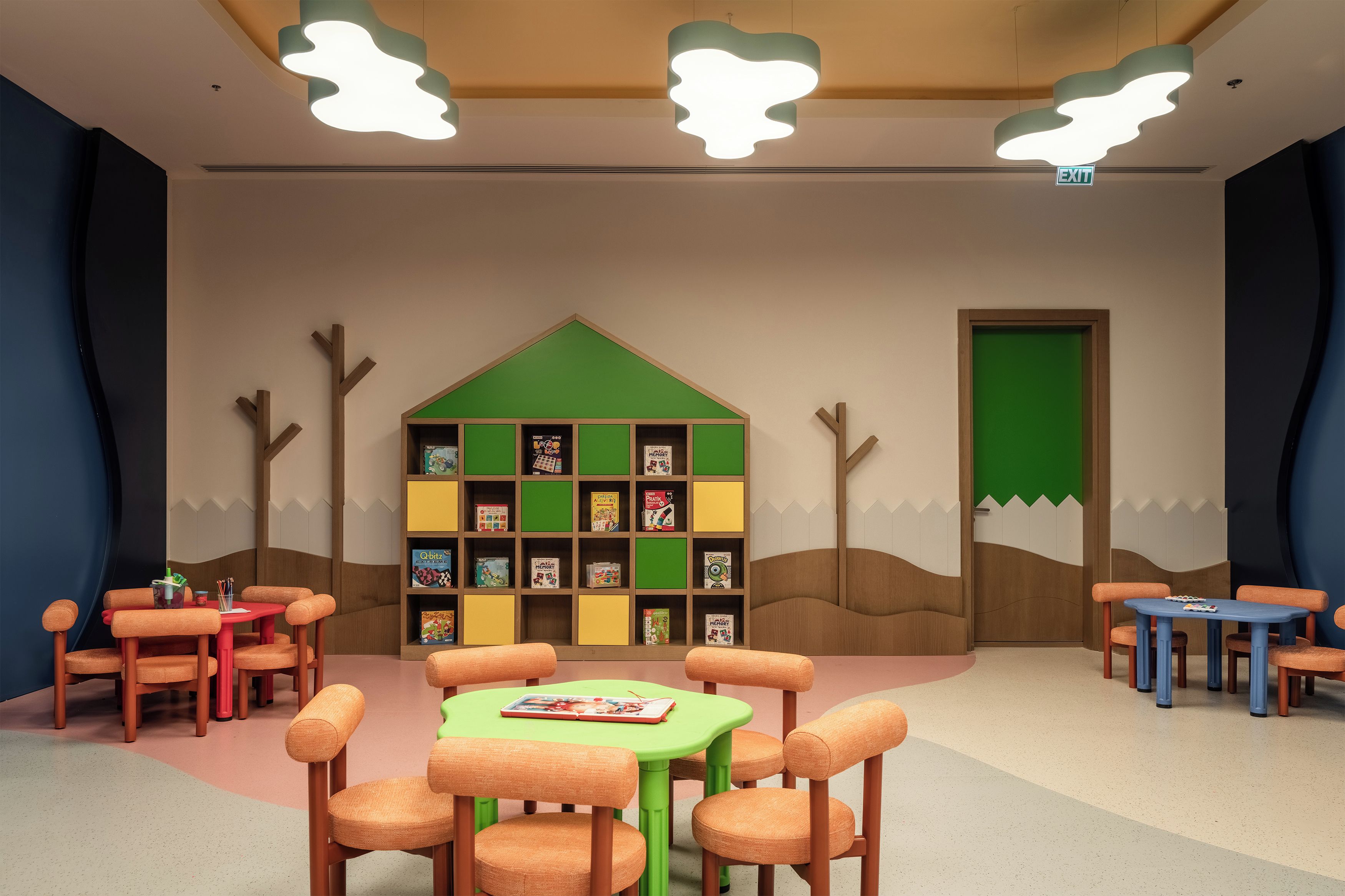 A children's playroom with a bookshelf, tables, chairs, and a door.