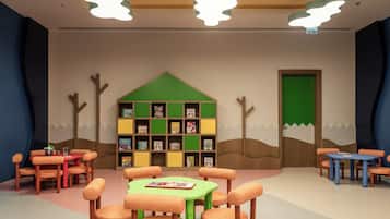 A children's playroom with a bookshelf, tables, chairs, and a door.